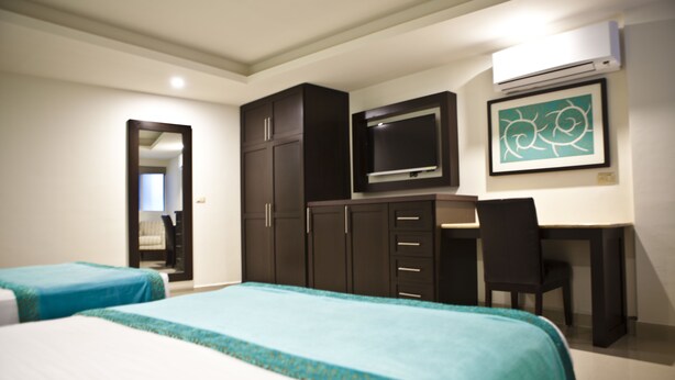 A hotel room with two beds, a desk, a chair, a television, and a framed artwork on the wall.