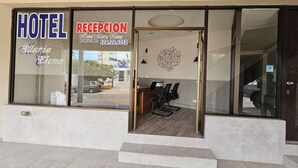 A hotel reception area with a reception desk, chairs, and a large window displaying the hotel's name and contact number.