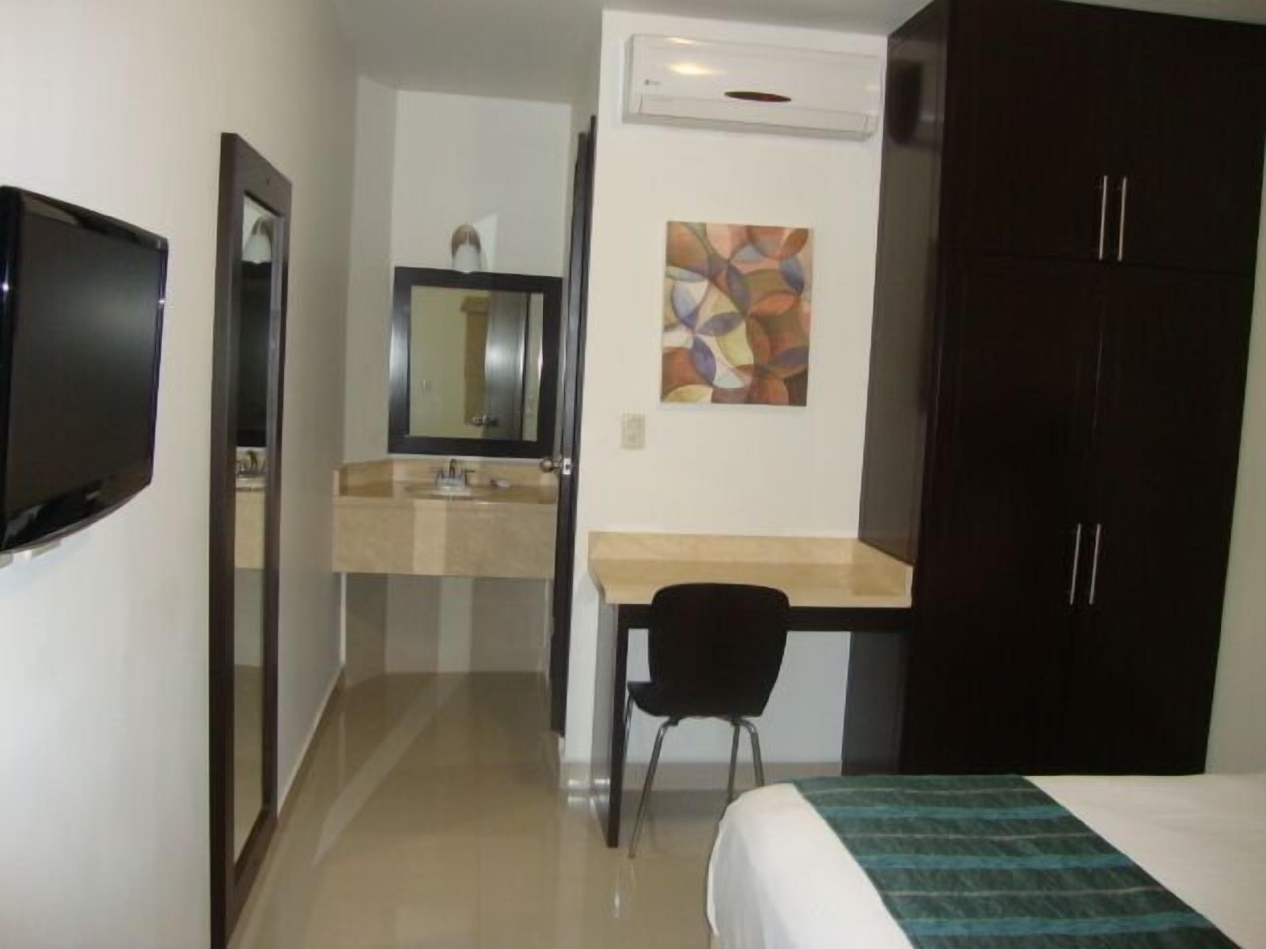Ein Hotelzimmer mit Bett, Schreibtisch mit Stuhl, Spiegel, Waschbecken und Fernseher.