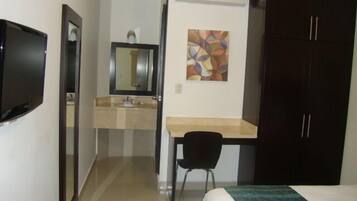 Ein Hotelzimmer mit Bett, Schreibtisch mit Stuhl, Spiegel, Waschbecken und Fernseher.