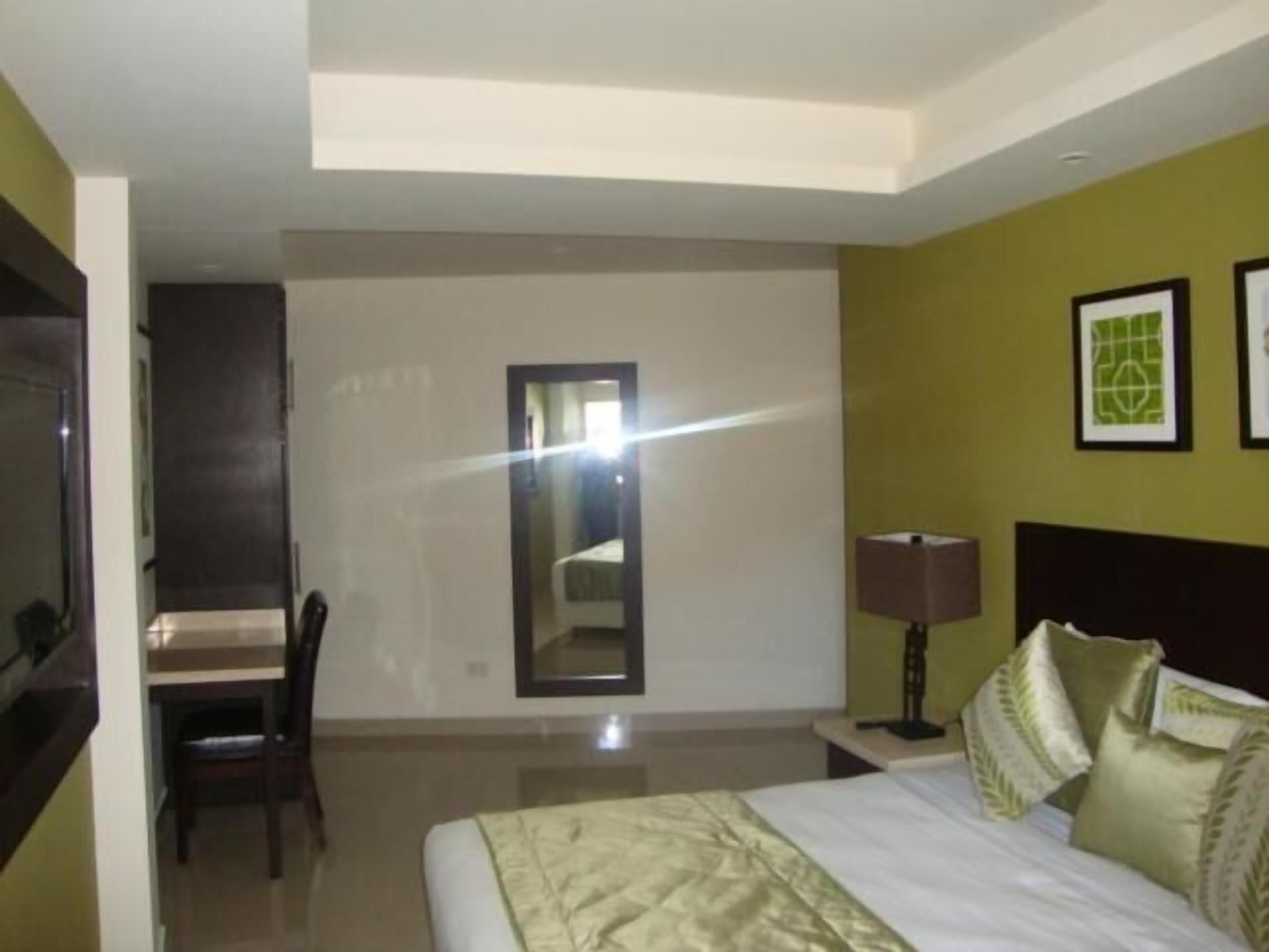 A hotel room with a bed, a chair, a desk, a lamp, and two framed pictures on the wall.