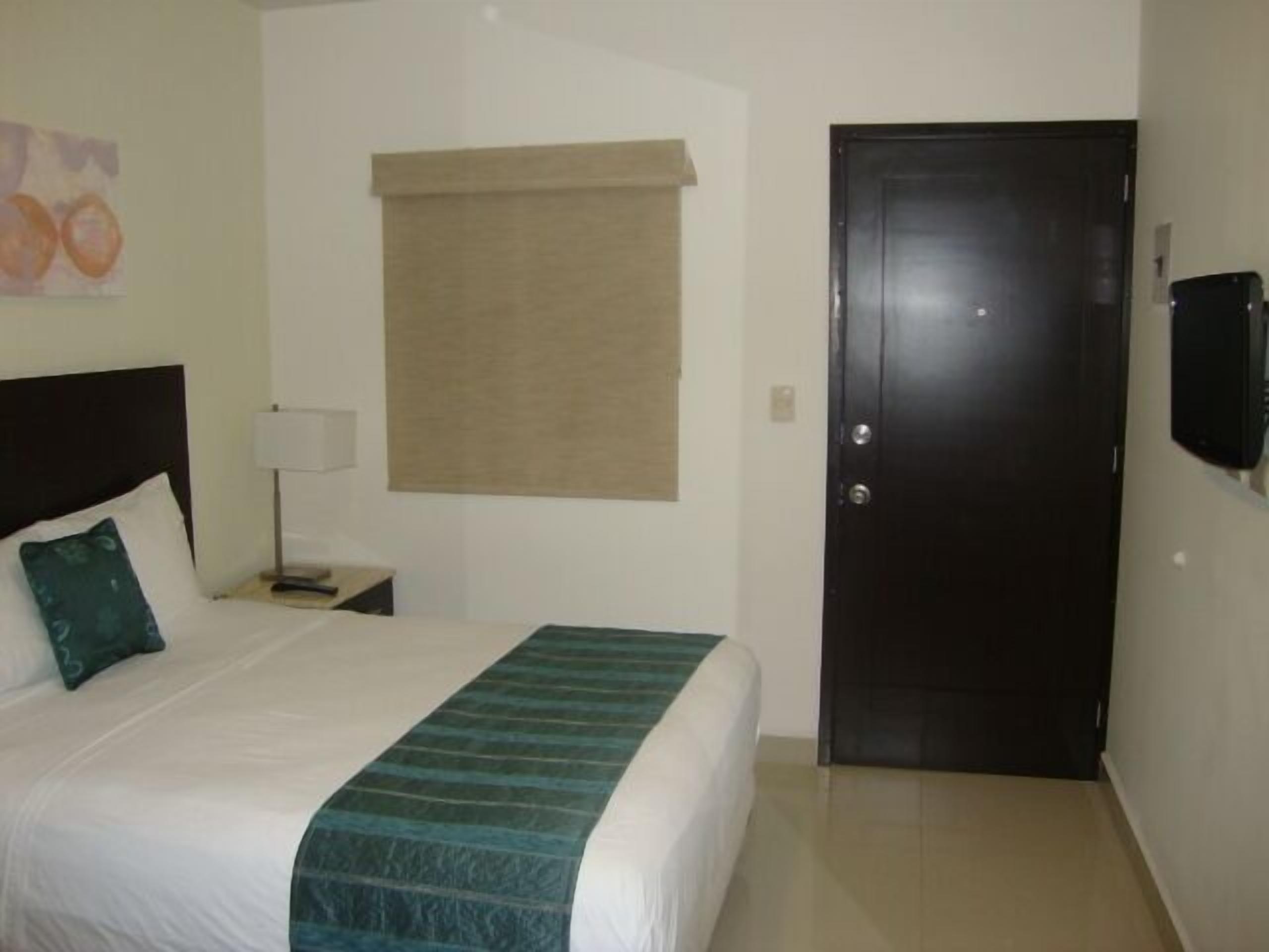 A hotel room with a bed, a nightstand, a lamp, a television, and a door.