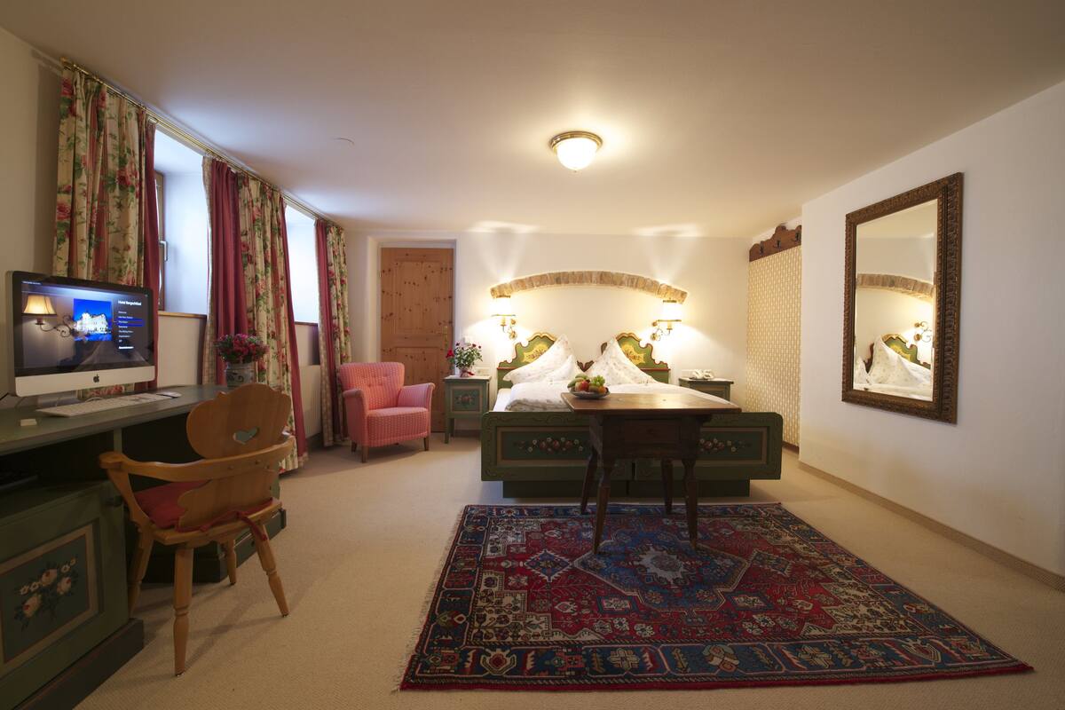 Un dormitorio con cama, escritorio, silla, televisor y un espejo grande.
