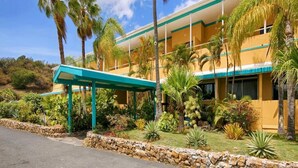 A hotel with a yellow facade, a covered entrance, and a garden with palm trees and various plants. - Lindbergh Bay Hotel and Villas (St. Thomas)