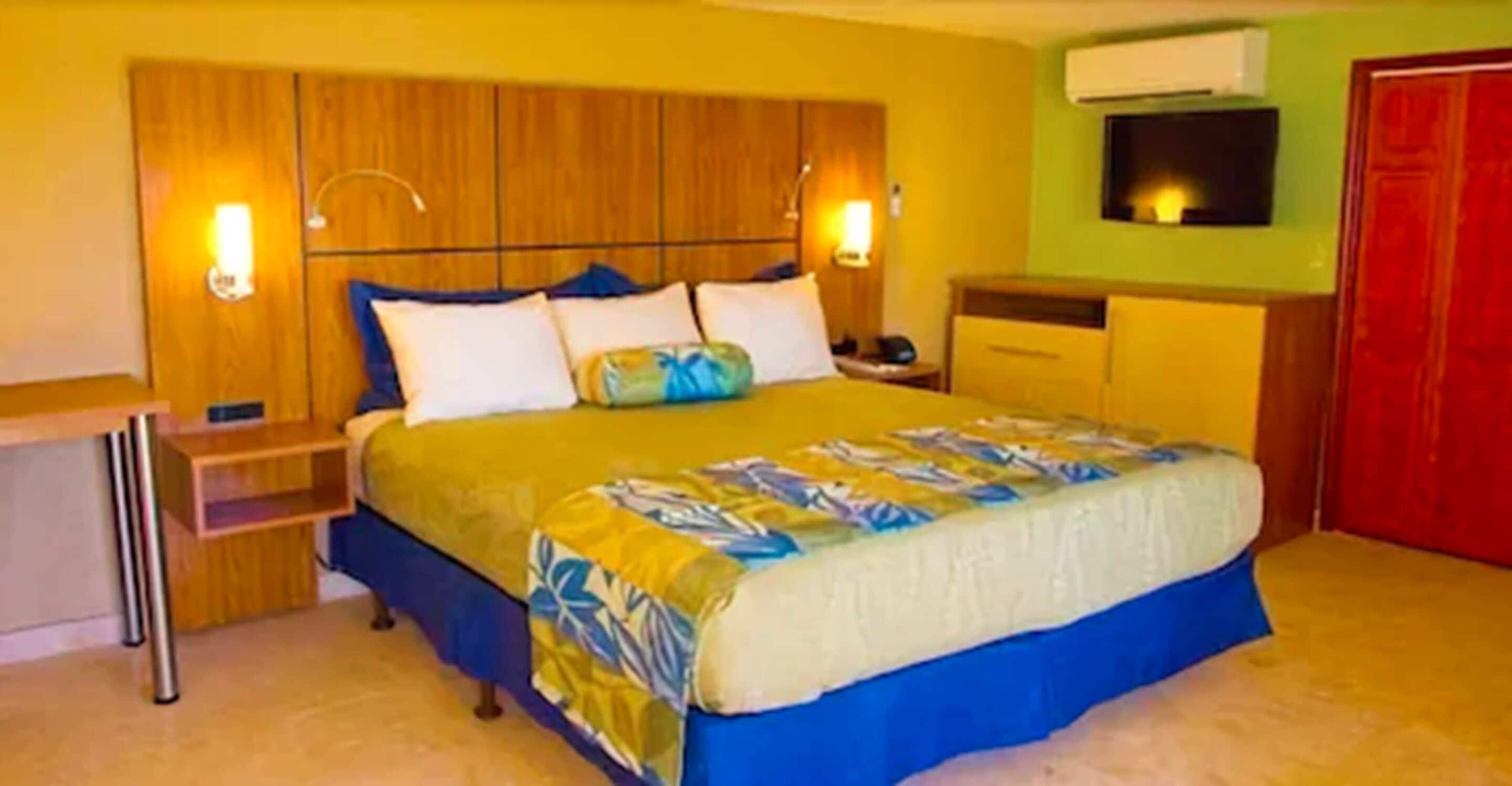 Quarto de hotel com cama, mesas de cabeceira, escrivaninha e guarda-roupa.