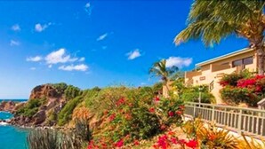 A coastal property with a view of the sea, a balcony with plants, and a building with a beige facade. - Lindbergh Bay Hotel and Villas (St. Thomas)