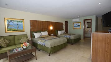 A hotel room with two beds, a green sofa, a small table with magazines, and a TV.