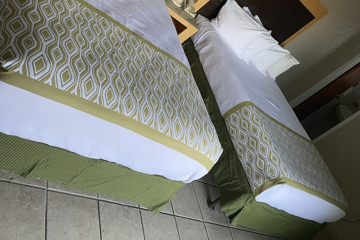 Zwei Betten mit gemusterten Bettbezügen, ein Nachttisch mit einer Lampe und ein Fliesenboden.