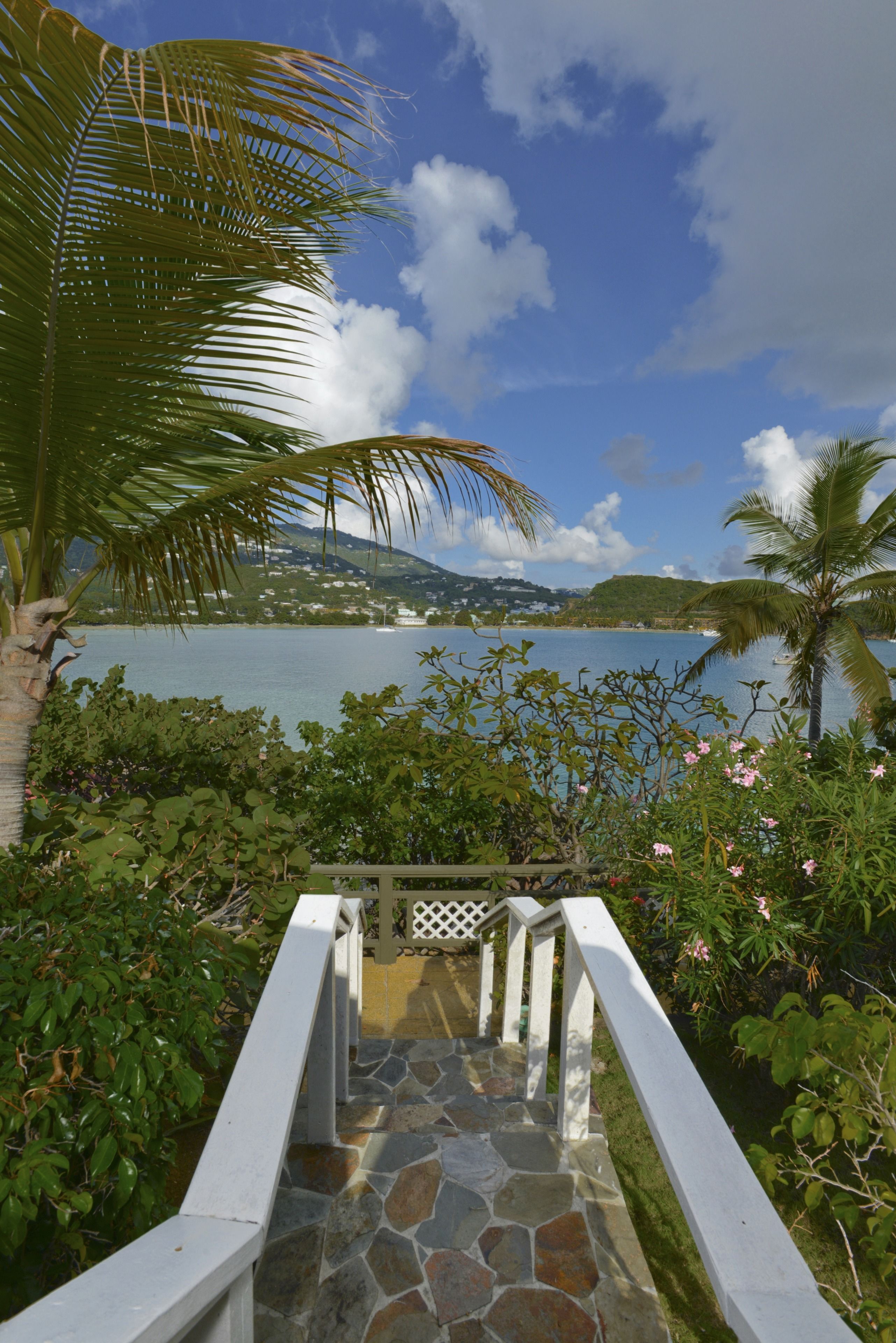 A stone staircase leading to a balcony overlooking a body of water, surrounded by lush greenery and a clear sky.