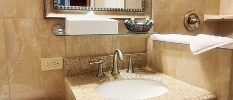 Bagno con lavabo su piano in granito, due rubinetti, ripiano in vetro sopra il lavabo, specchio e water.