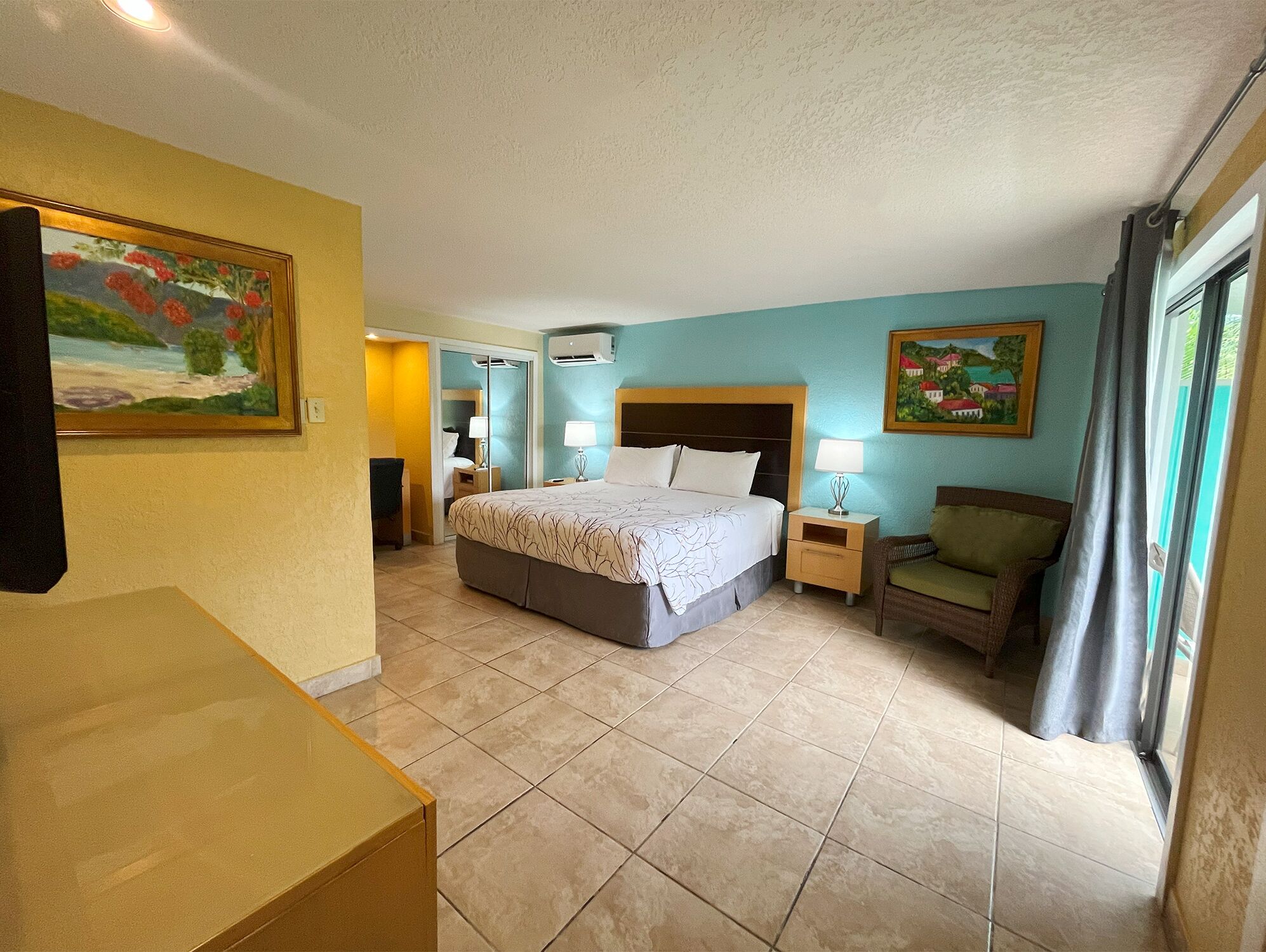 A hotel room with a bed, a chair, a desk, and a painting on the wall.