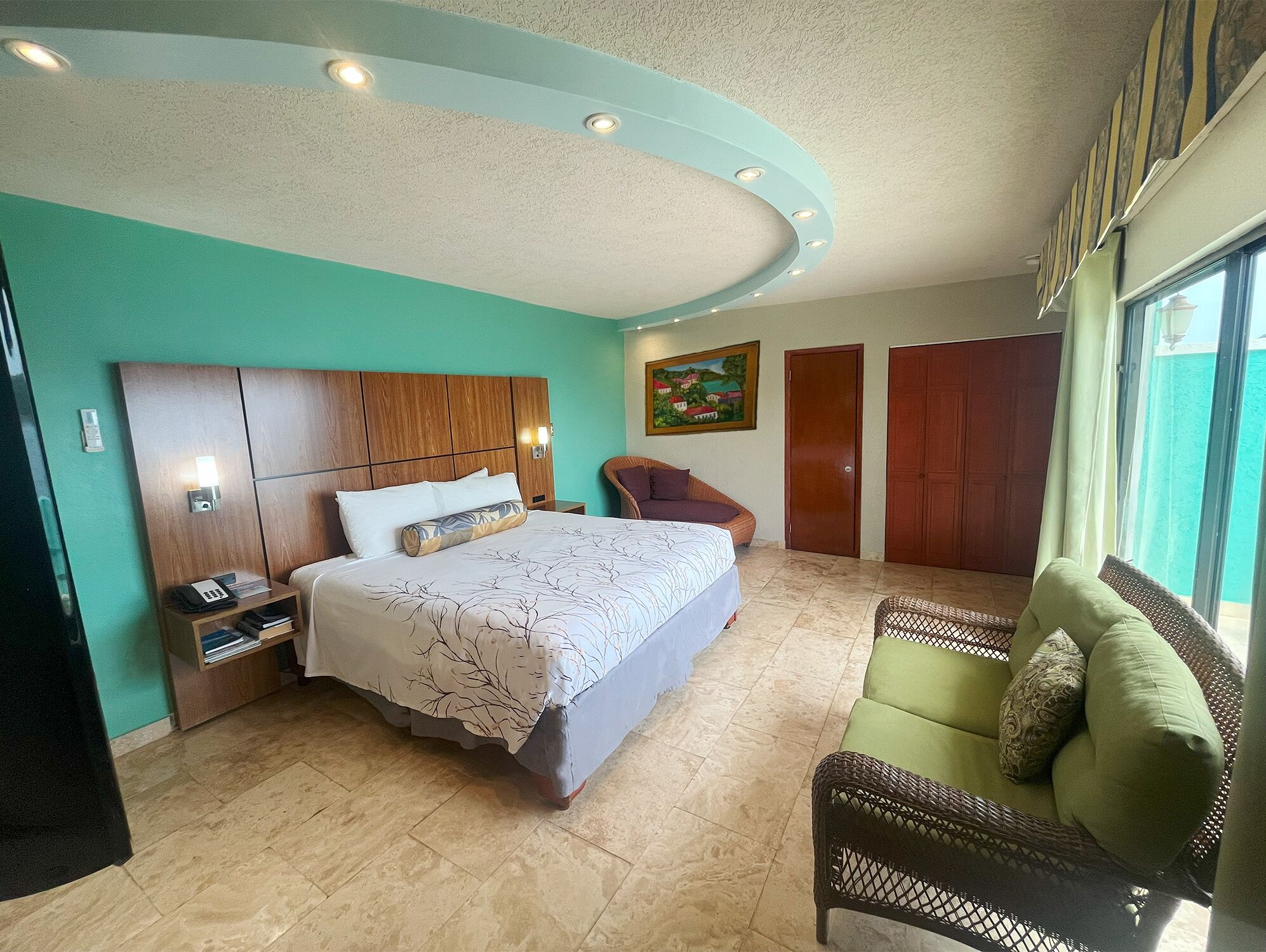 A hotel room with a bed, a chair, a nightstand, and a painting on the wall.