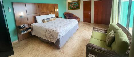 A hotel room with a bed, a chair, a nightstand, and a painting on the wall.