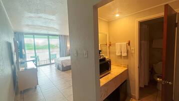 A hotel room with a balcony, a bathroom with a shower, and a dining area.
