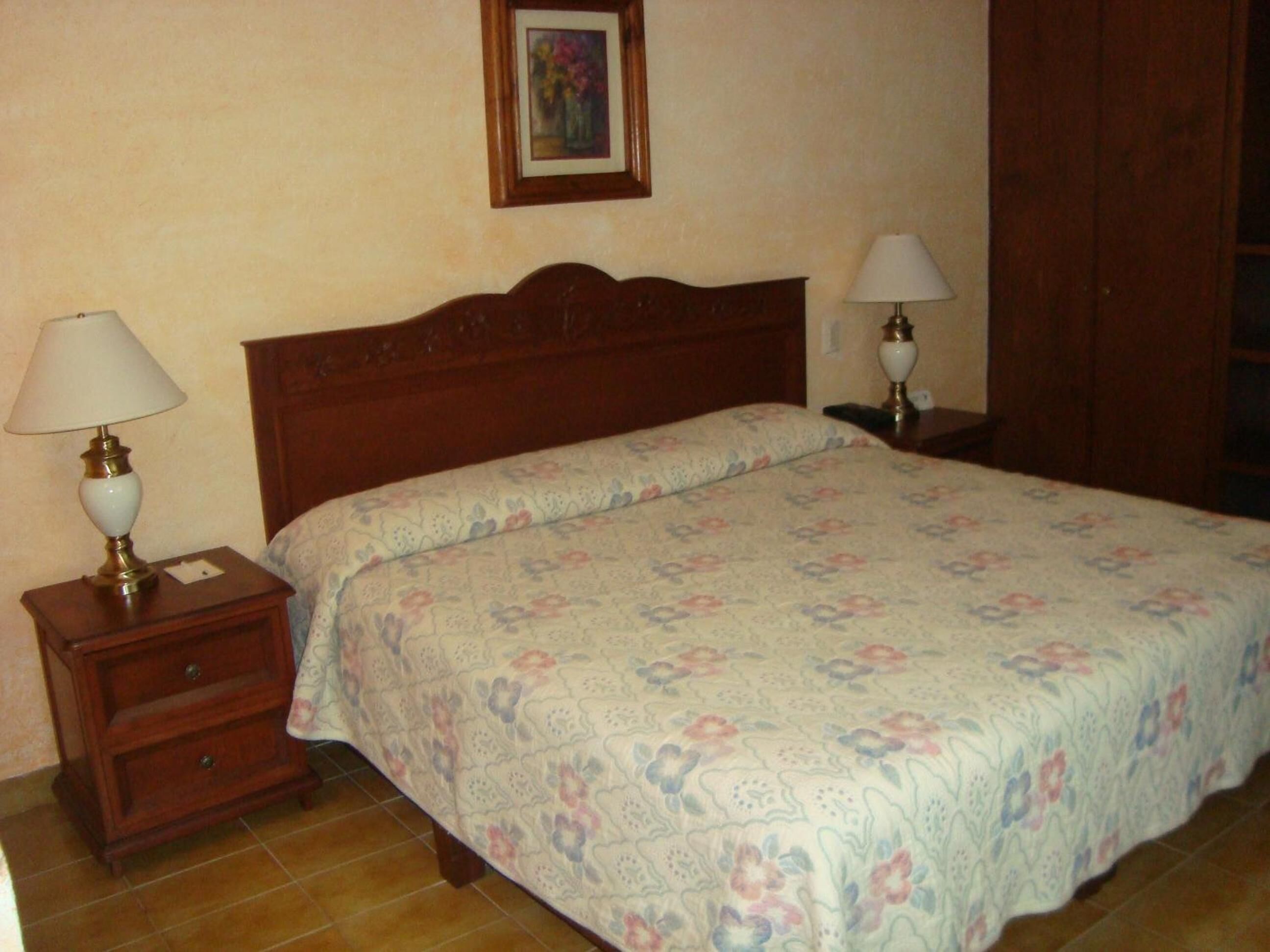 A bedroom with a wooden bed, floral bedding, two bedside tables with lamps, and a framed picture on the wall.