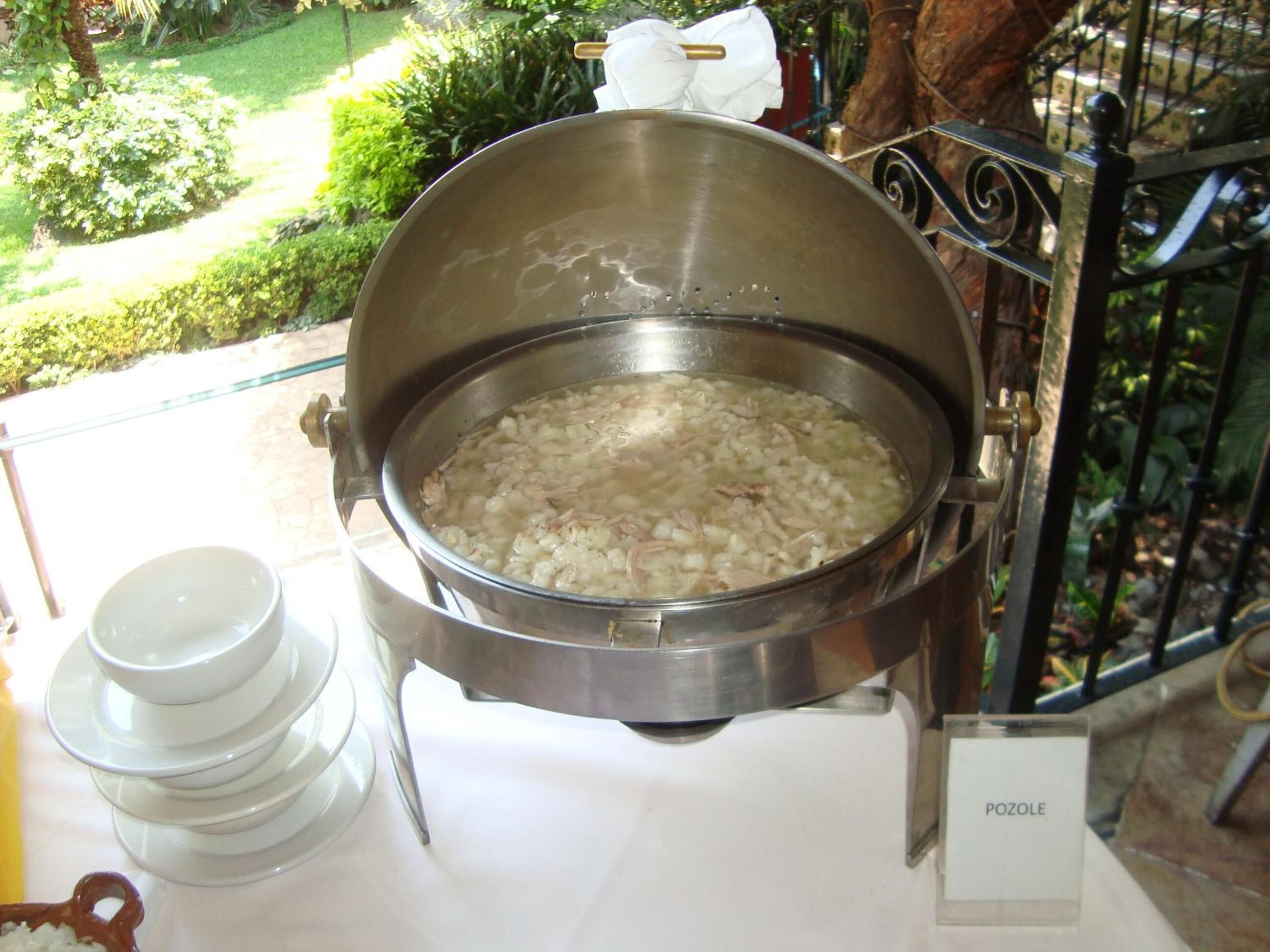 A large pot of soup on a table with a sign labeled "POZOLE".