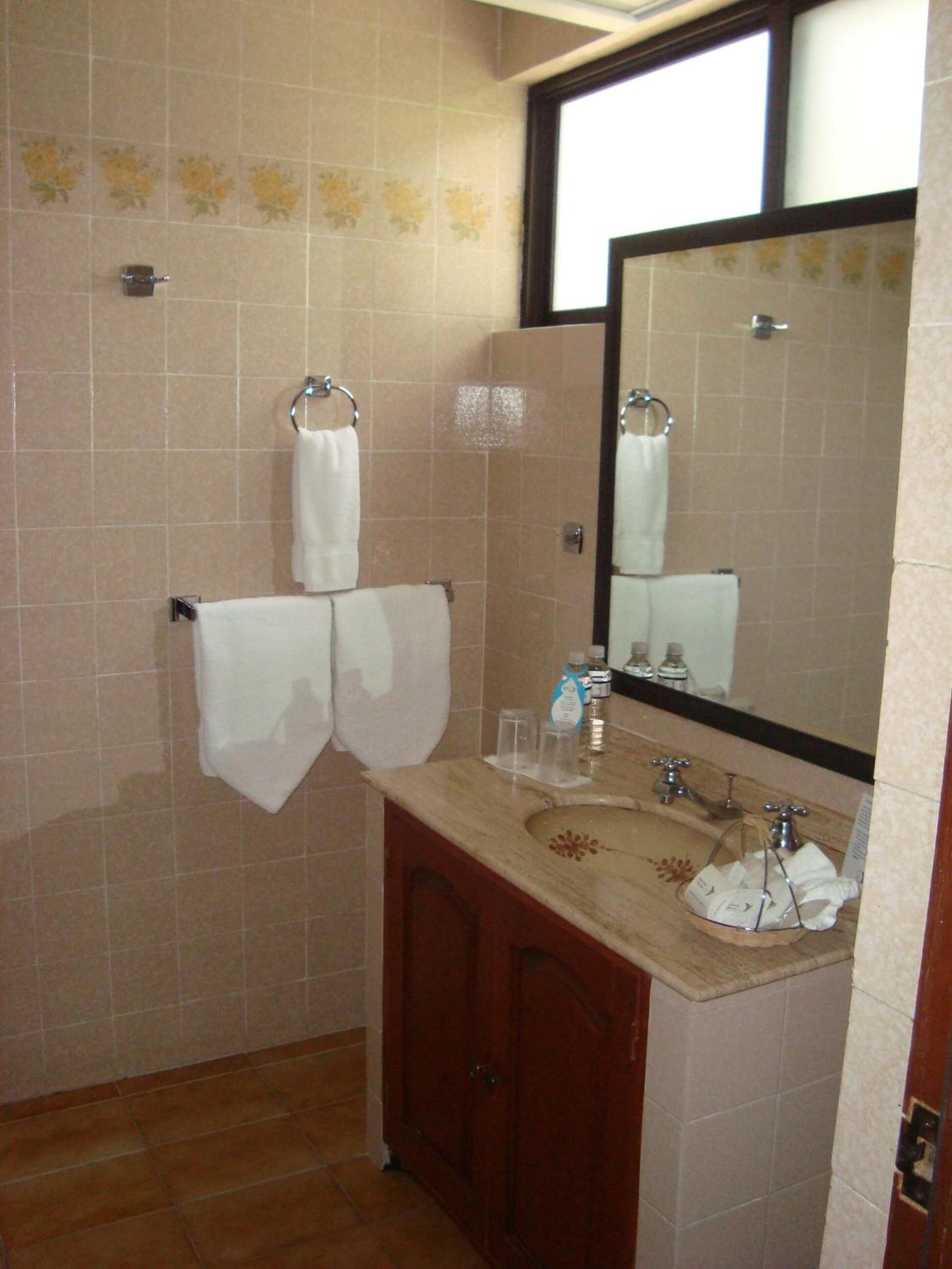 A bathroom with beige tiles, a wooden cabinet, a sink with a mirror, and two towels hanging on hooks.