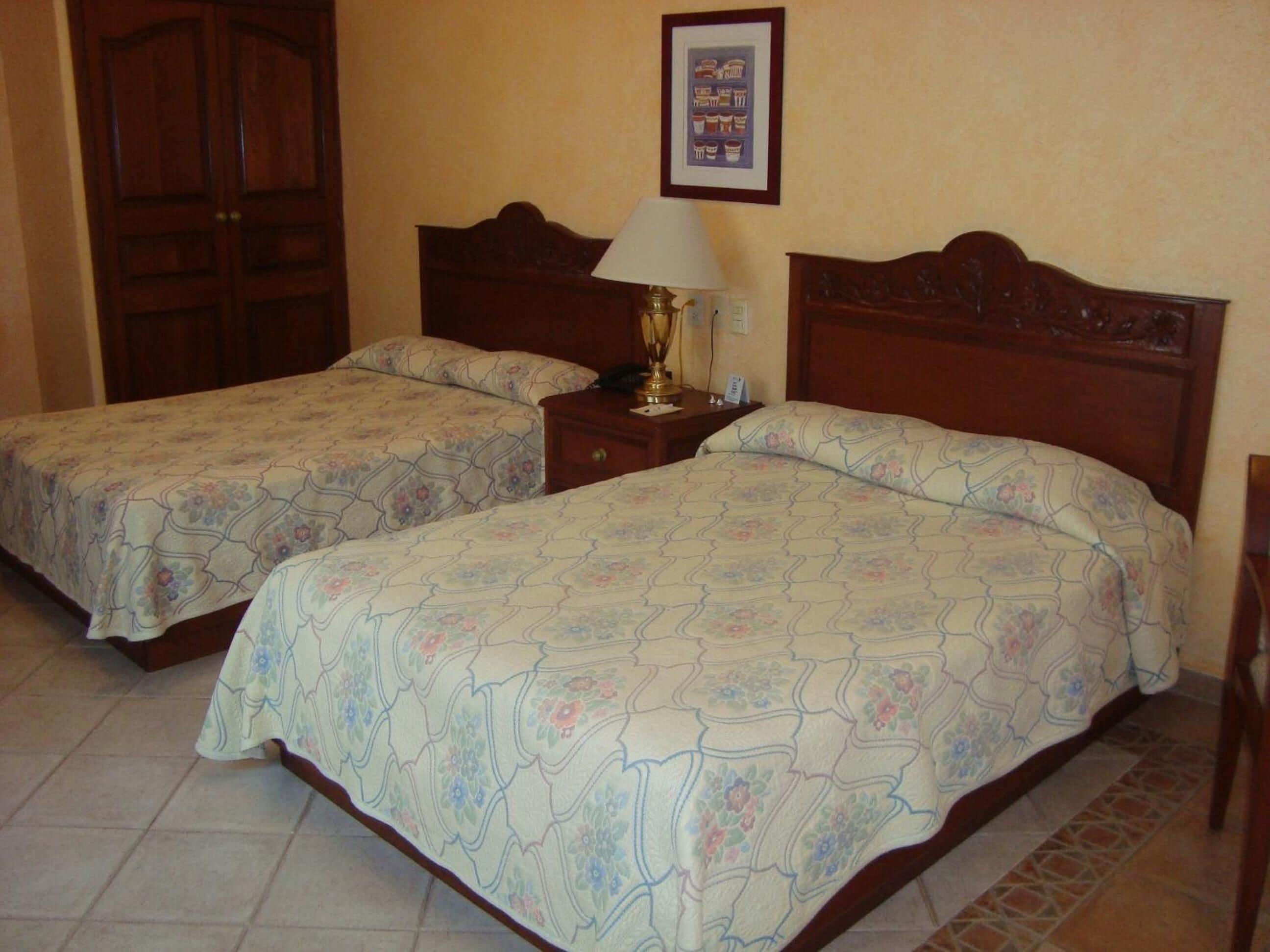 Quarto de hotel com duas camas, uma mesa de cabeceira, um abajur e um quadro na parede.