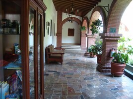 Un patio cubierto con suelo de piedra, un banco de madera, plantas en macetas y una chimenea de ladrillo.