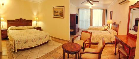 A hotel room with two beds, a wooden desk, a chair, a ceiling fan, and a painting on the wall.