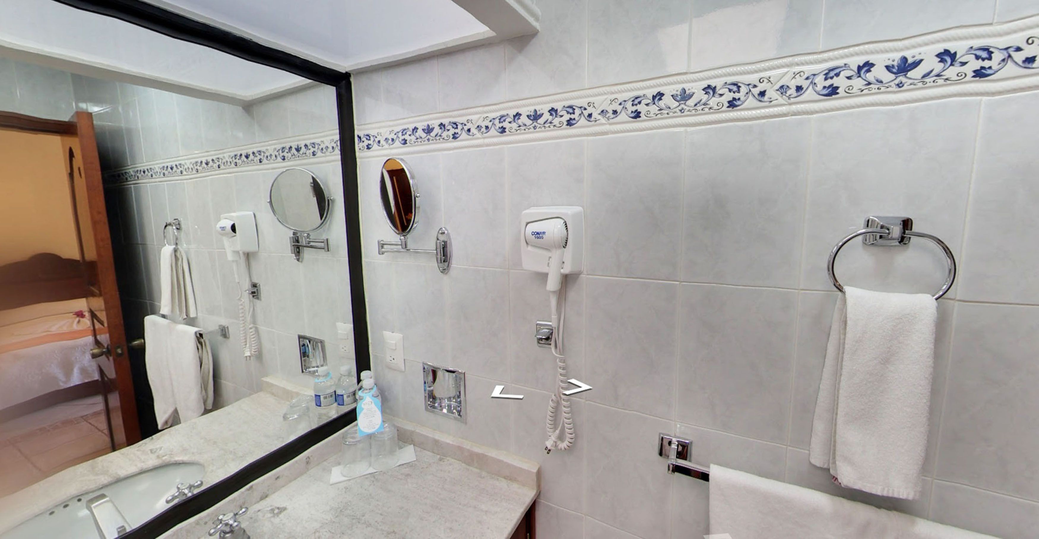 A bathroom with a large mirror, a sink, a towel ring, and a hairdryer.