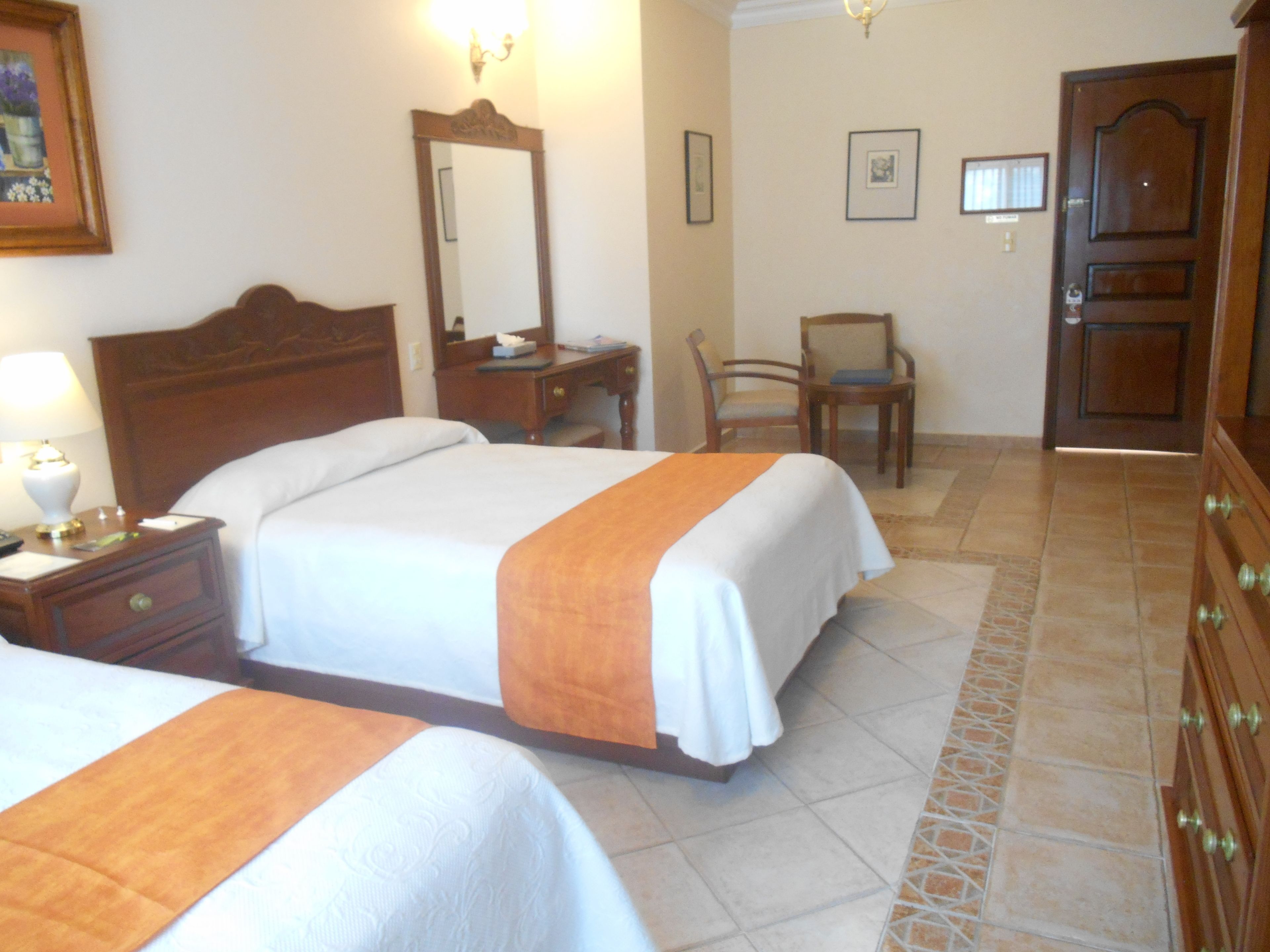 A hotel room with two beds, a wooden dresser, a chair, and a desk.