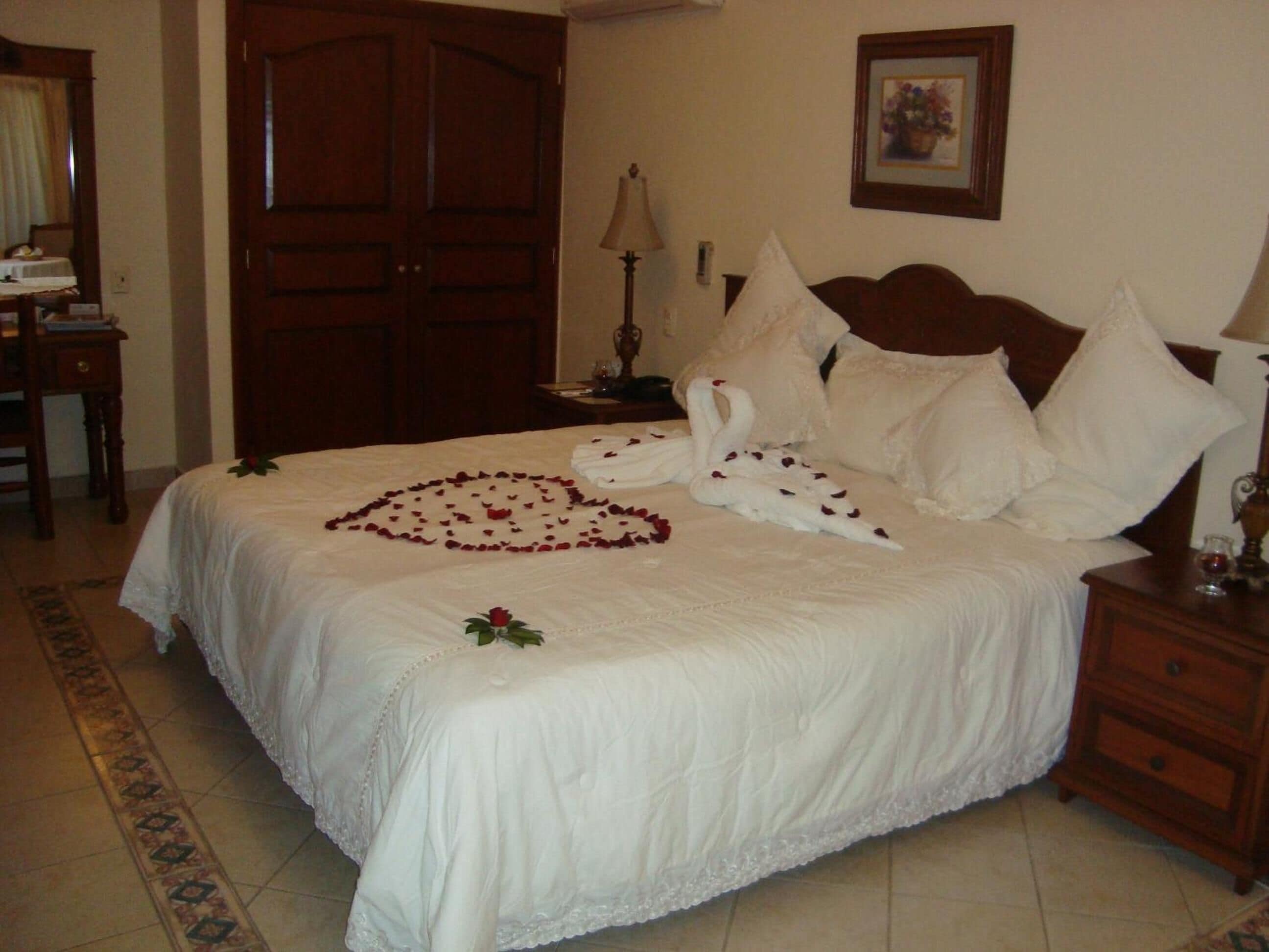 A neatly made bed with a heart-shaped arrangement of rose petals and a swan design on the bedspread.
