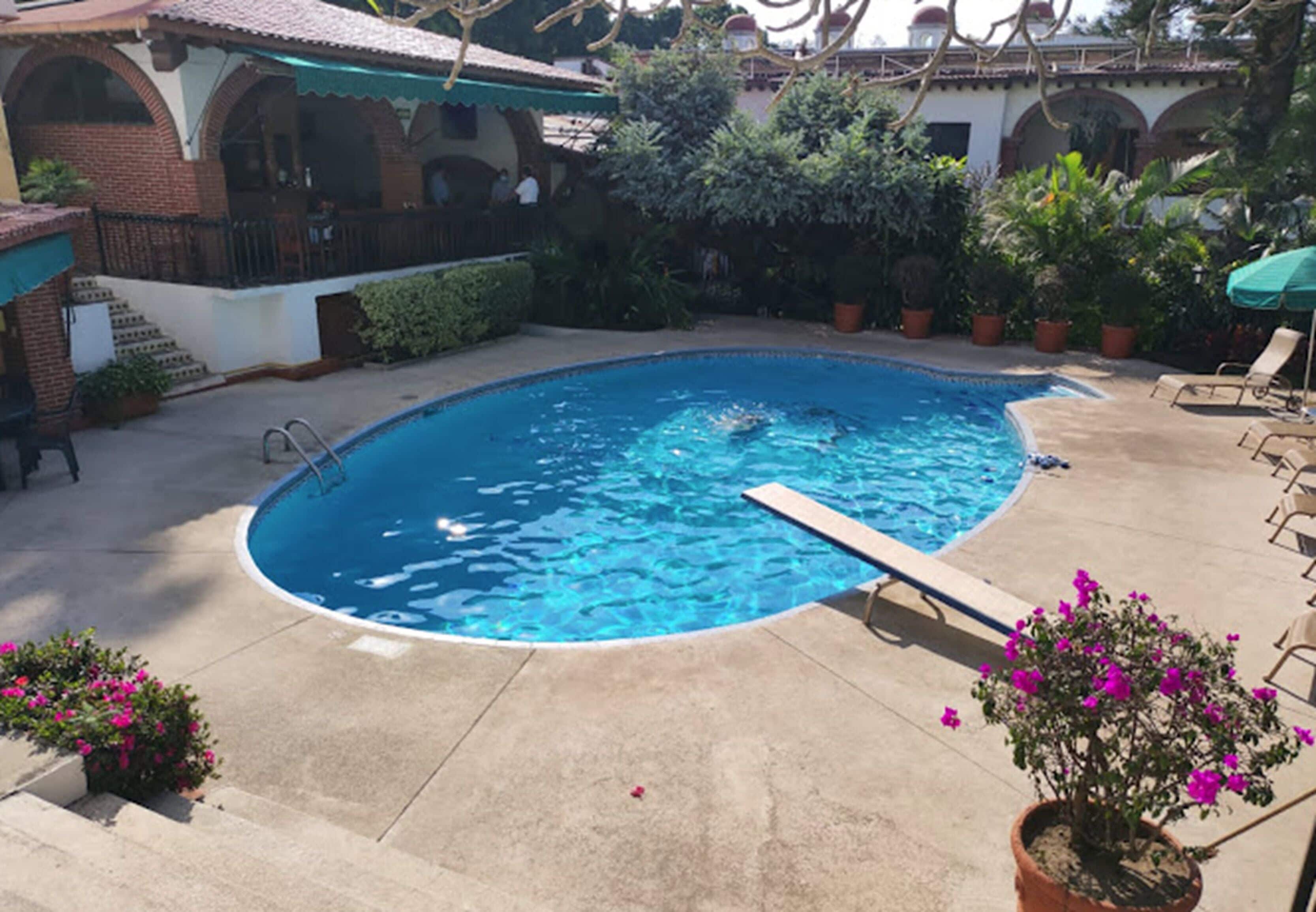 Ein Schwimmbecken mit Holzterrasse, umgeben von Blumentöpfen und Gartenmöbeln.