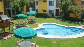 A swimming pool surrounded by outdoor seating and umbrellas, with a building in the background.