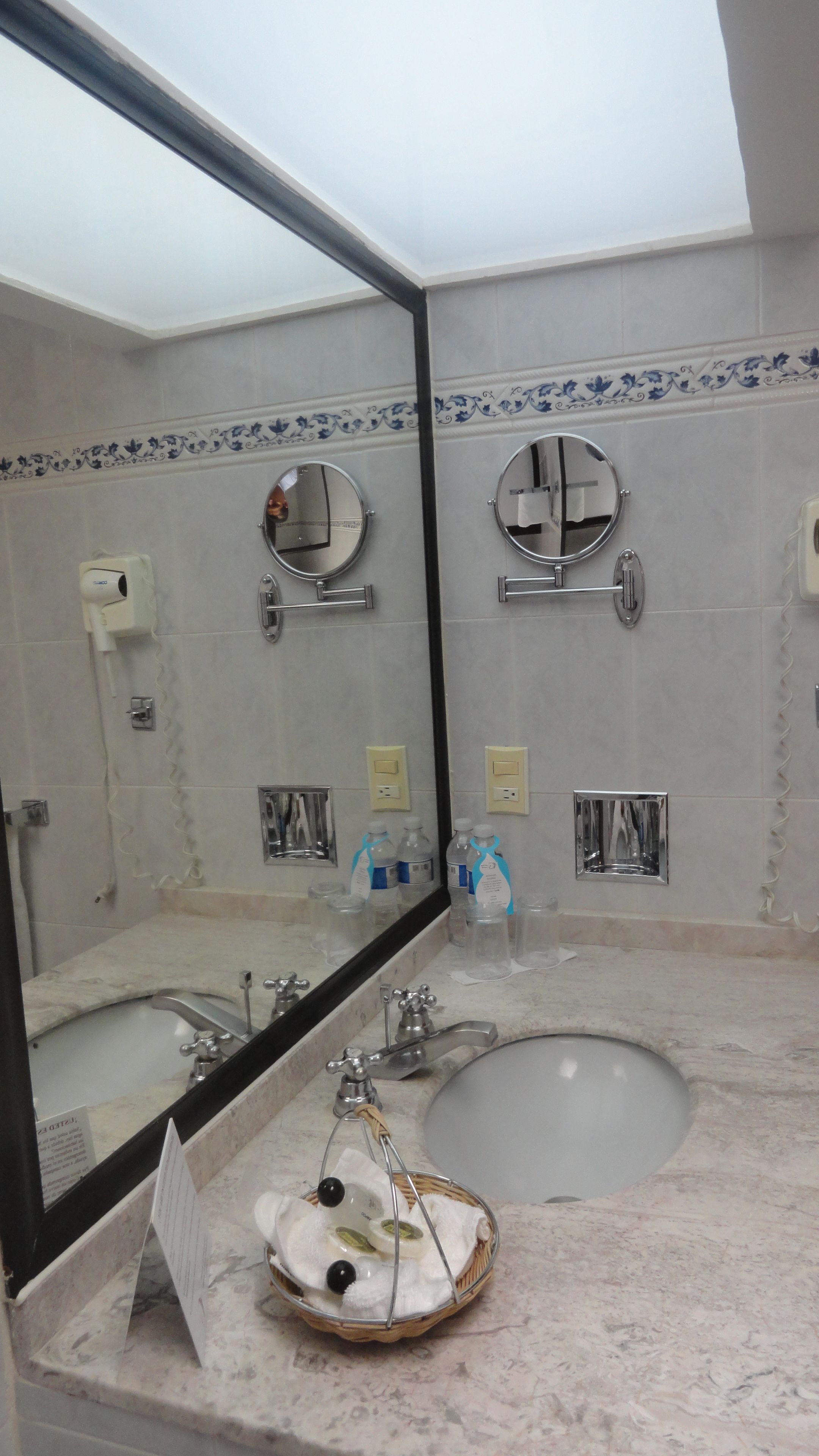 Une salle de bain avec un grand miroir, deux lavabos, un meuble-lavabo et un luminaire au plafond.