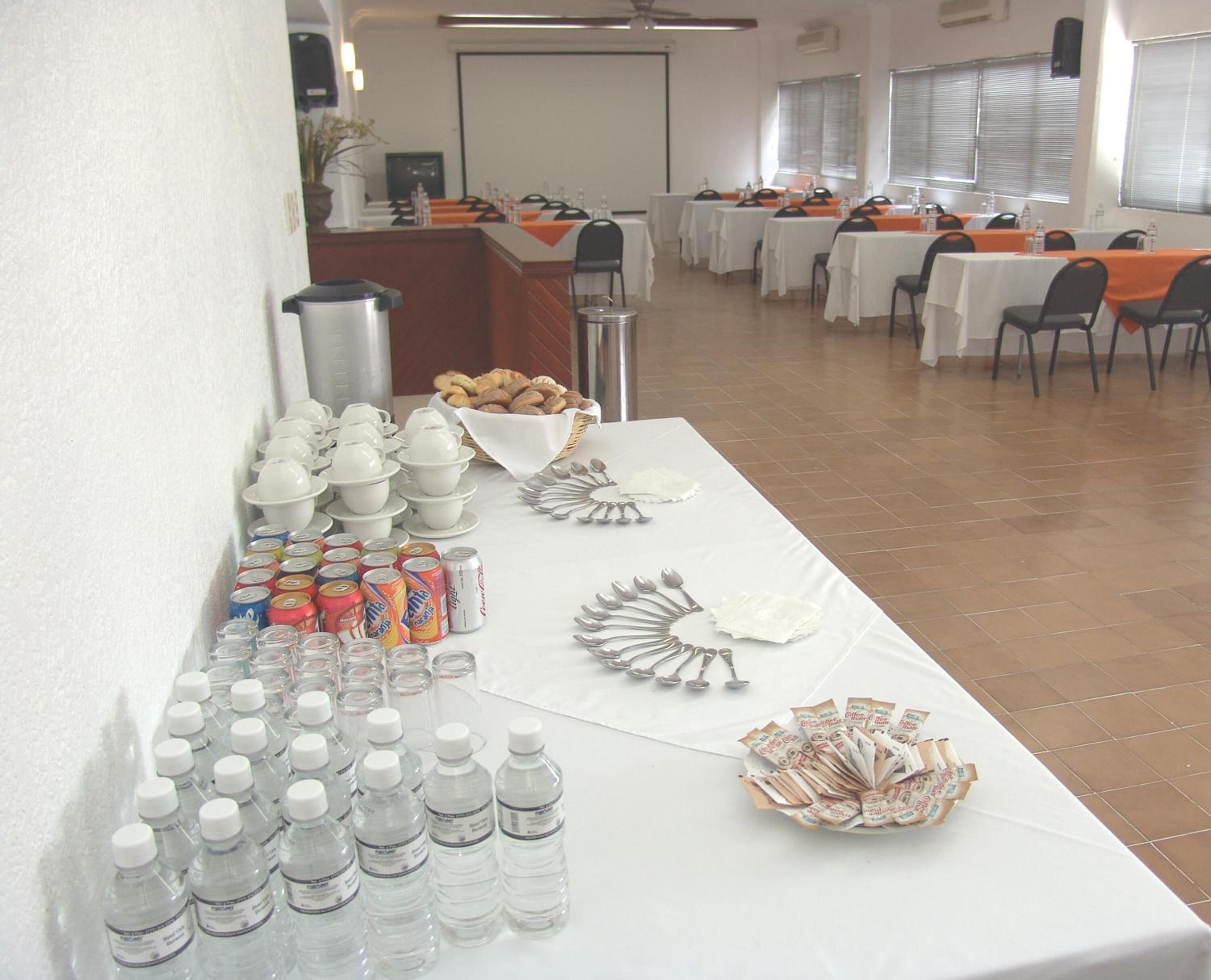 Une salle de conférence avec des tables préparées pour une réunion, équipée de bouteilles d’eau, de gobelets et d’un buffet de viennoiseries.