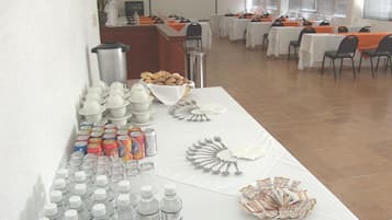 Une salle de conférence avec des tables préparées pour une réunion, équipée de bouteilles d’eau, de gobelets et d’un buffet de viennoiseries.