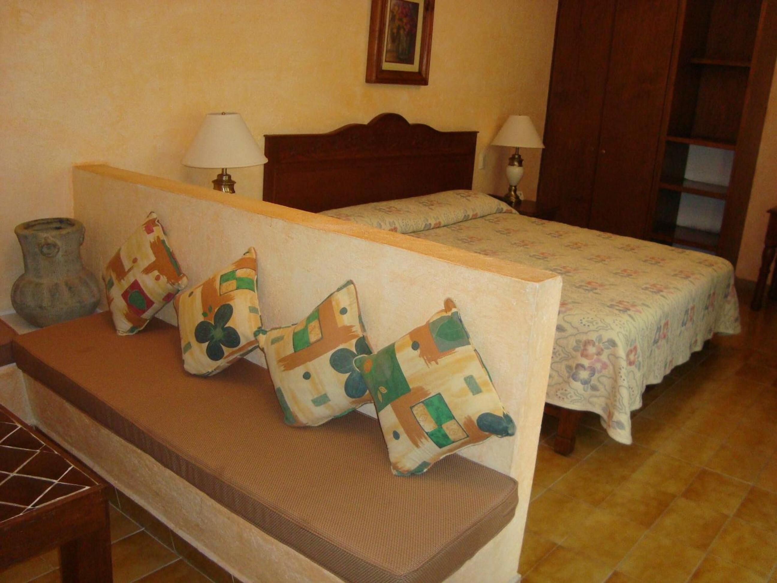 A bedroom with a bed, two bedside lamps, a wooden headboard, and a bench with cushions.