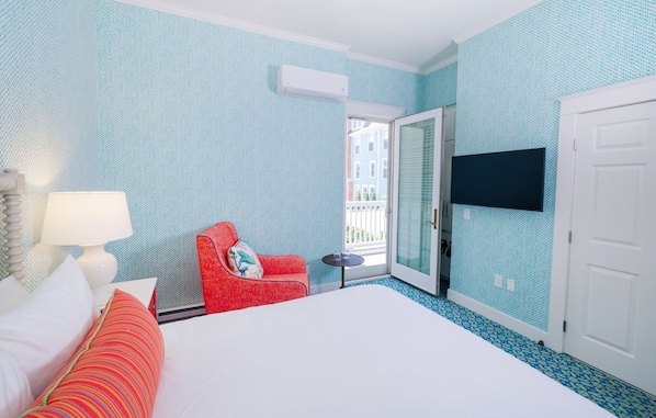 A hotel room with a bed, a red armchair, a small table, a TV mounted on the wall, and a balcony door. - Harbour View Inn (Mackinac Island)