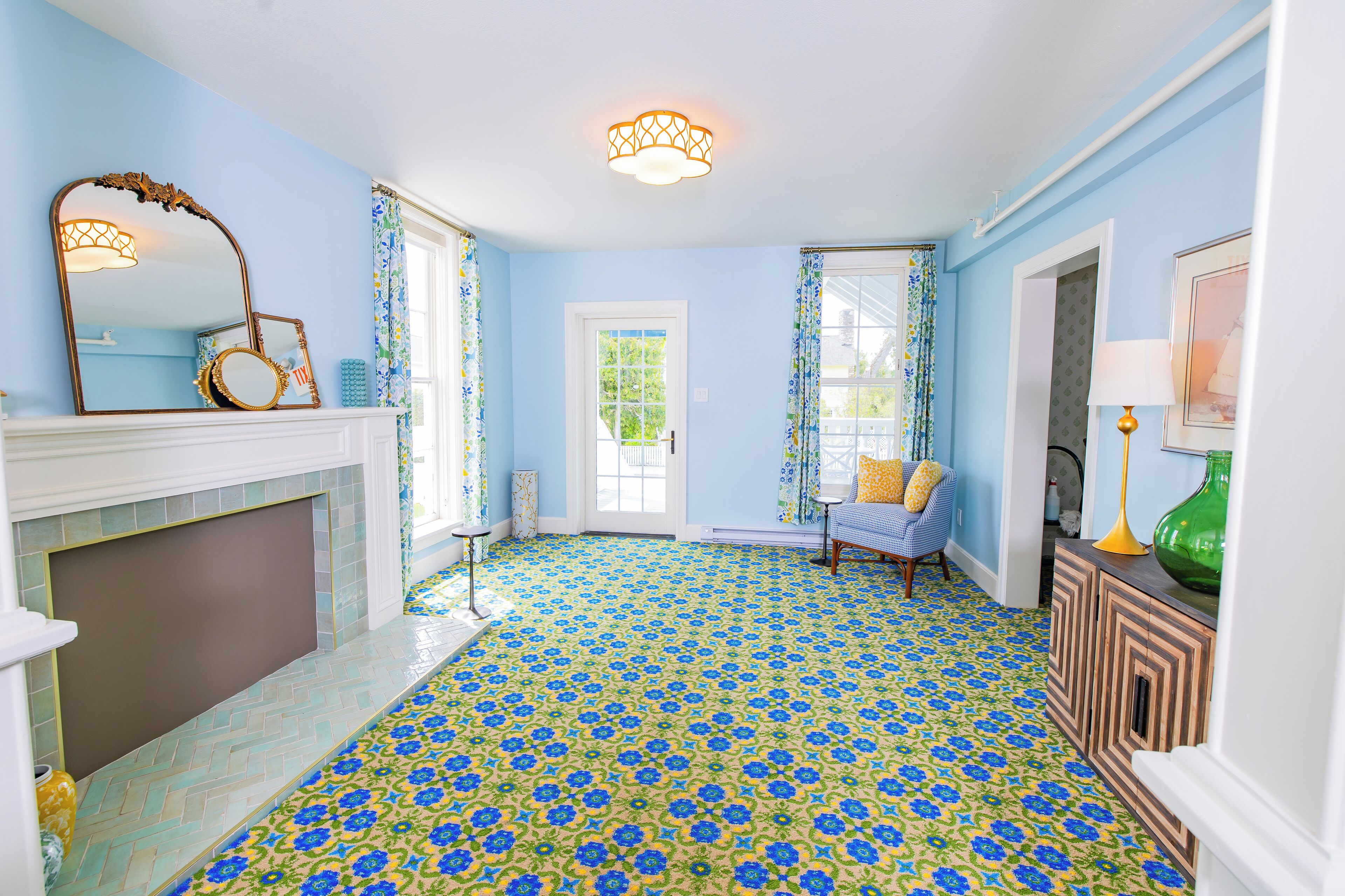 Une pièce avec un sol à motifs floraux bleus, une cheminée, un miroir et une fenêtre avec des rideaux.