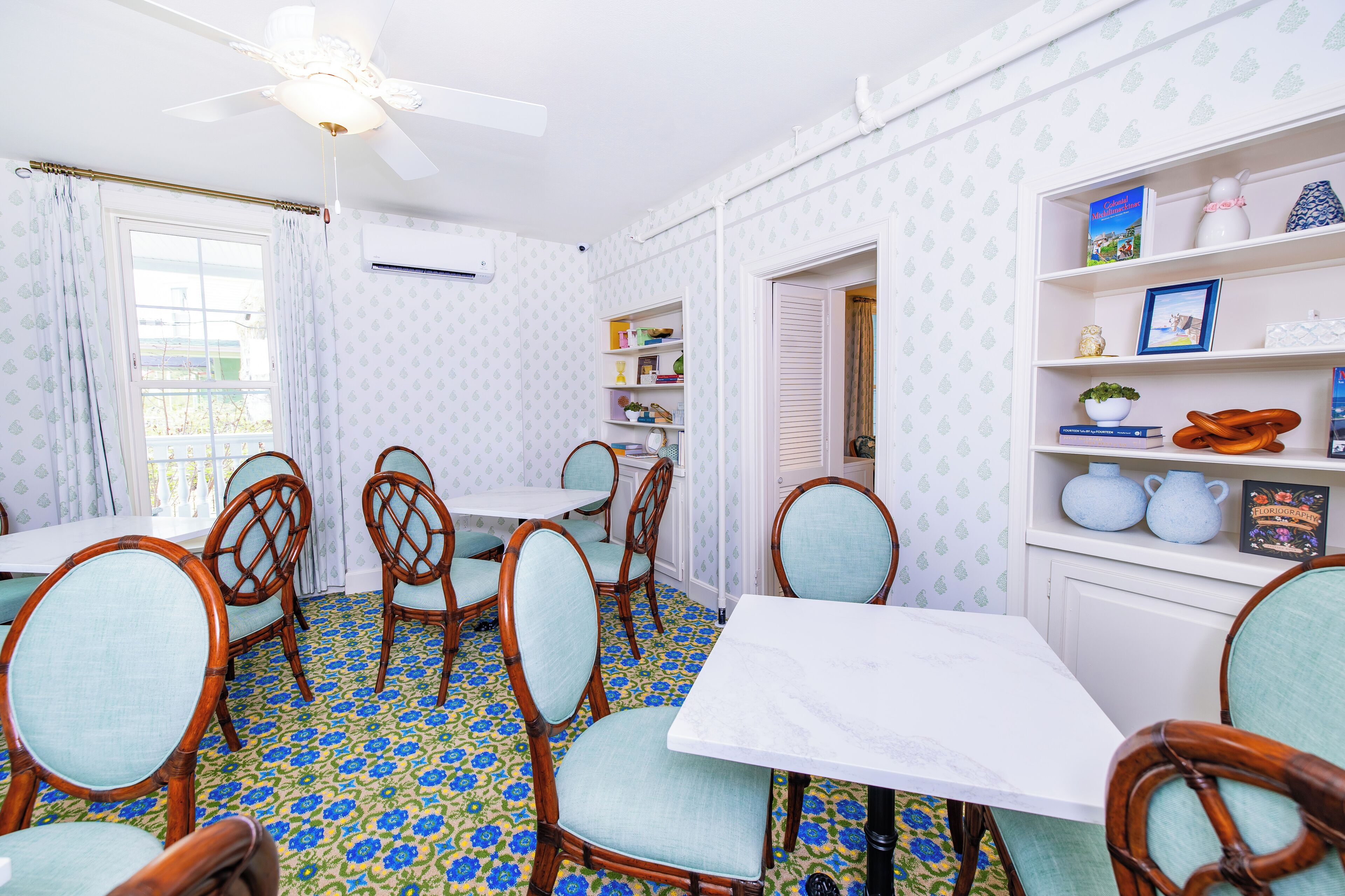 A dining area with wooden chairs and a white table, a ceiling fan, and patterned wallpaper.