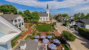 A church with a steeple, surrounded by residential houses, a well-maintained lawn, and outdoor seating with umbrellas.