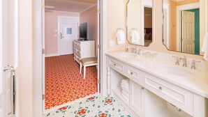 A hotel bathroom with two sinks, a large mirror, and a vanity with drawers.