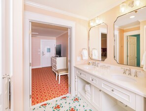 A hotel bathroom with two sinks, a large mirror, and a vanity with drawers.