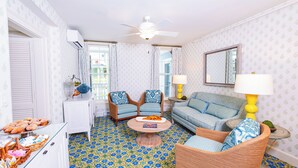A living room with patterned floor tiles, a ceiling fan, a sofa, two armchairs, a coffee table, and a side table with a lamp.