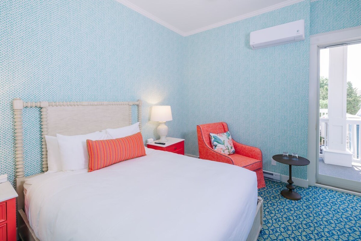A hotel room with a bed, a red chair, a small table, and a window with a view.