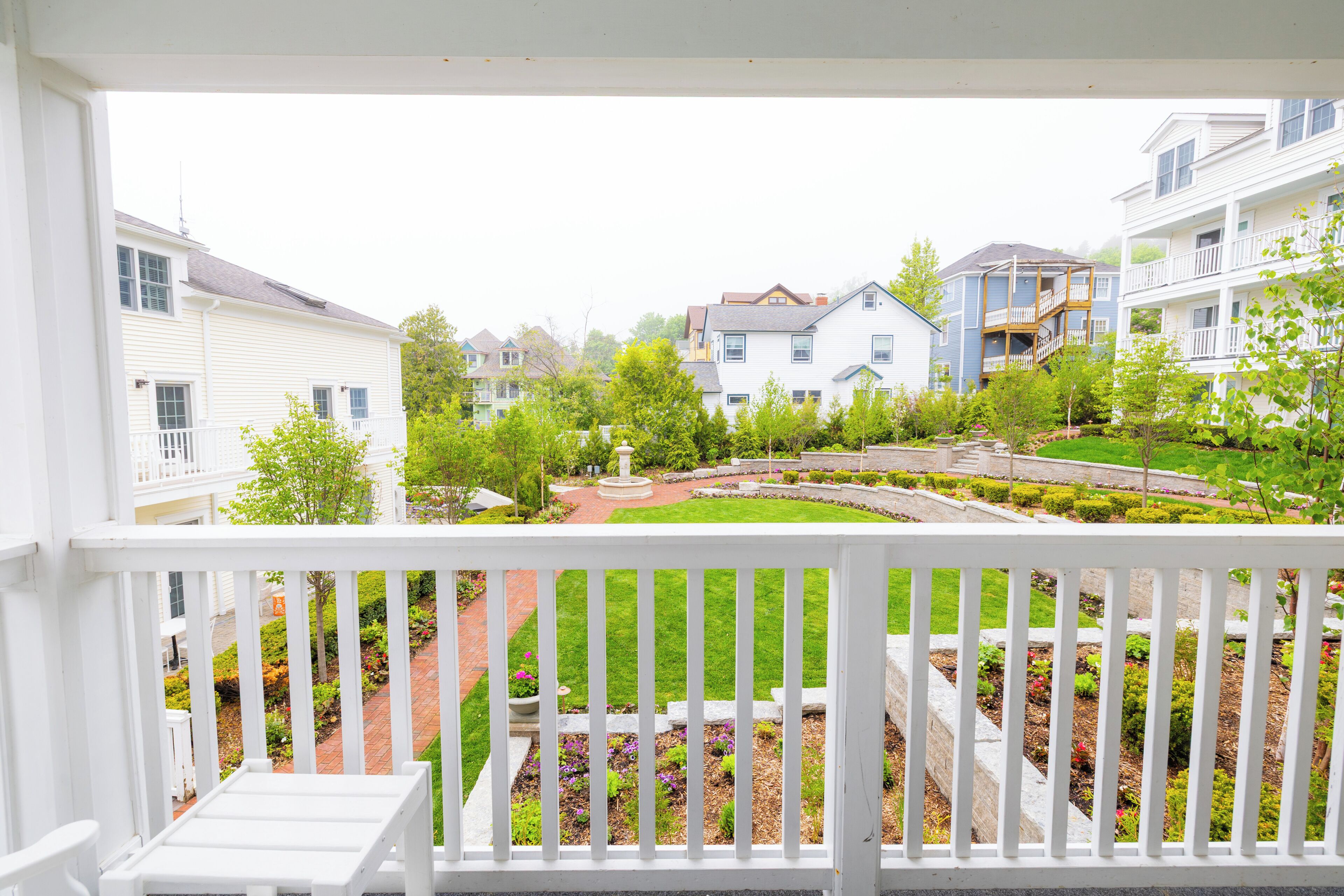A residential area with white houses, a well-maintained garden, and a white balcony railing.