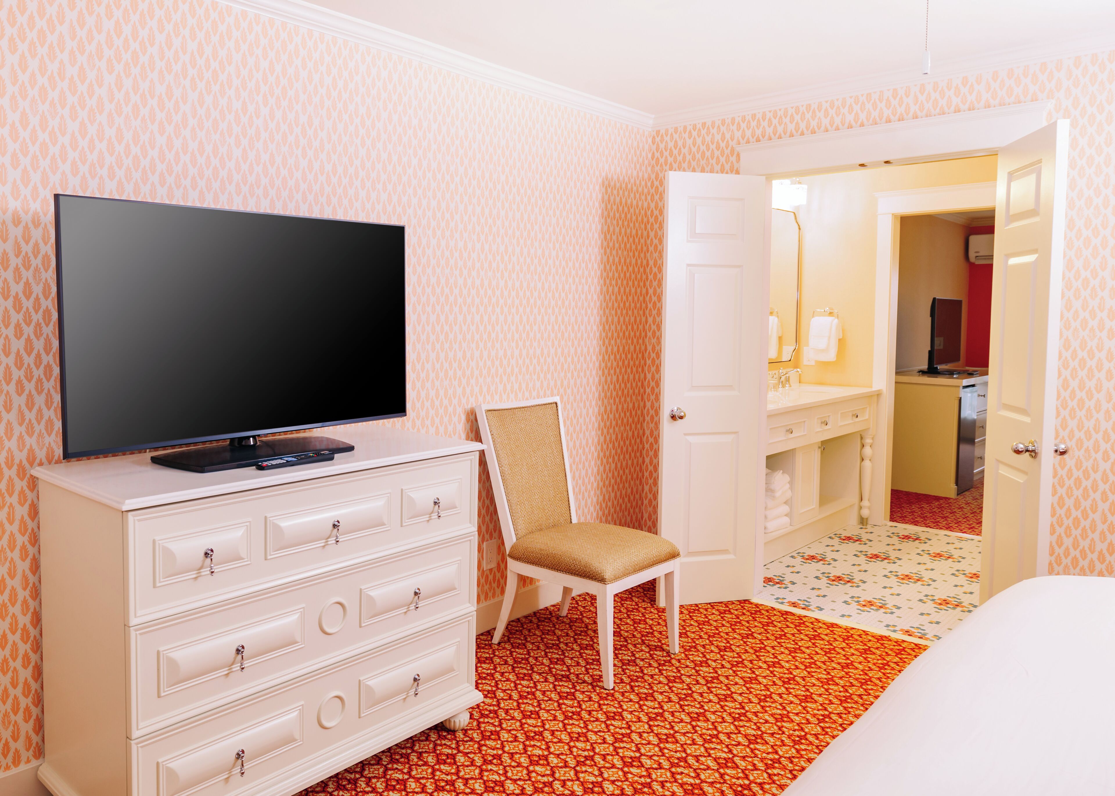 A hotel room with a television on a dresser, a chair, a bed, and a bathroom visible through an open door.
