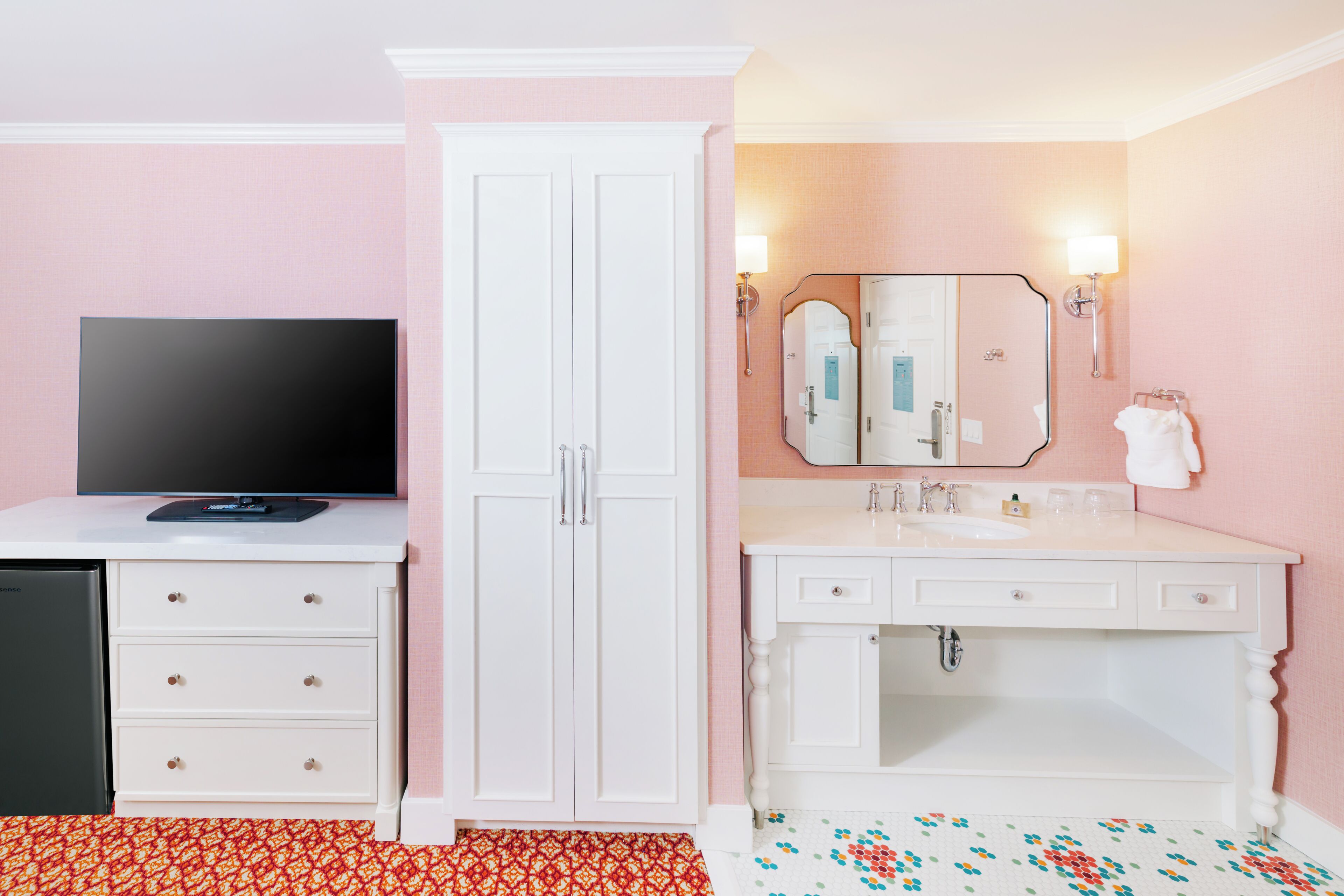 A hotel room with a television, wardrobe, and bathroom with a mirror and sink.