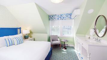 A hotel room with a bed, a chair, a small table, a vanity with a mirror, and a window.