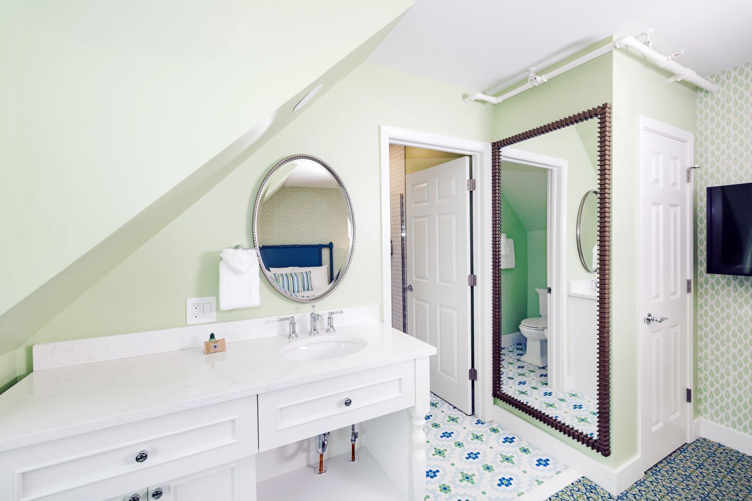 Een badkamer met een wit wastafelmeubel, een ronde spiegel en een douchegedeelte met een bruine deur.