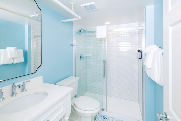 Un baño moderno con un lavamanos, inodoro y ducha blancos, y una pared de acento azul.