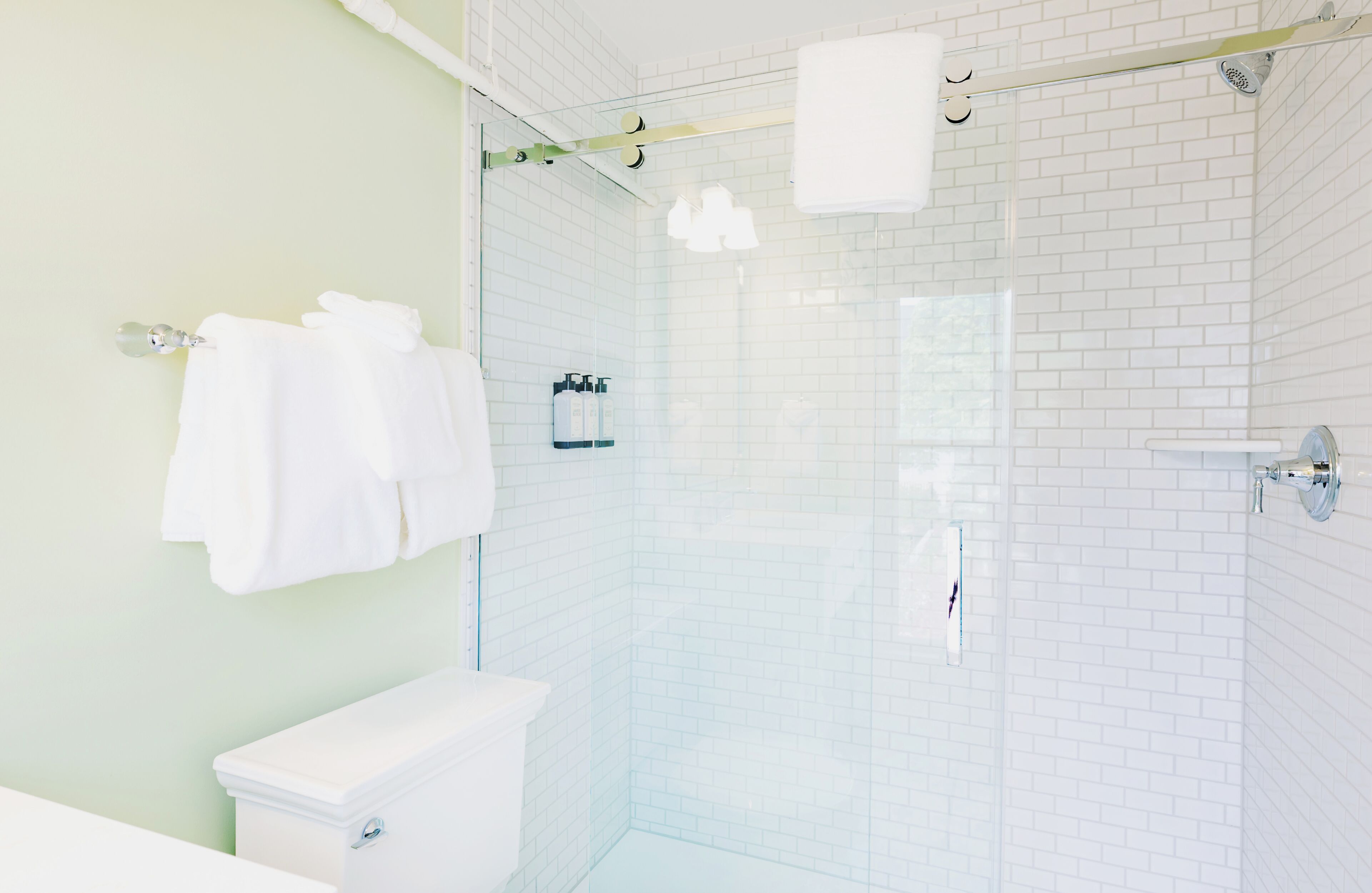 A bathroom with a glass shower enclosure, white tiles, a toilet, and a towel rack.