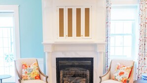 Una habitación con chimenea, dos sillones con cojines estampados, una mesita de centro con una bandeja decorativa y un suelo con diseño.