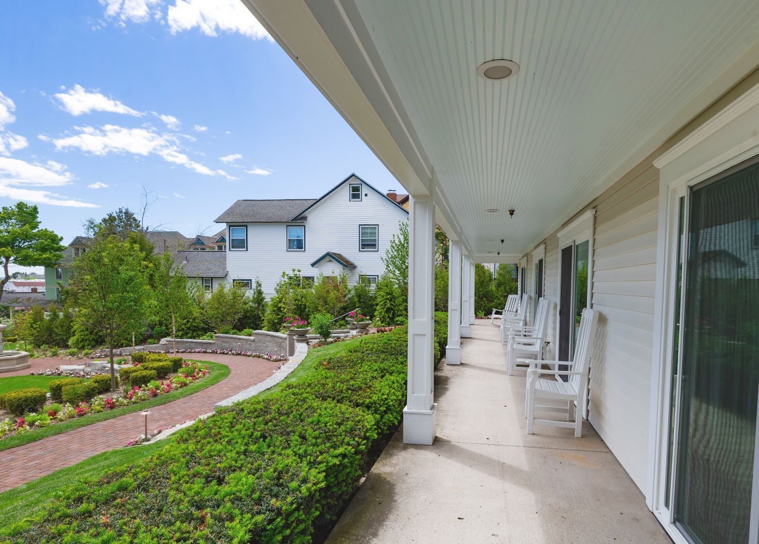 A covered porch with white chairs, a brick pathway, and a well-maintained garden.